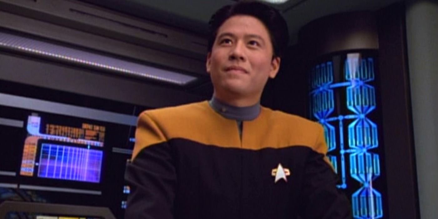 Harry Kim from Star Trek: Voyager stands at his station on the USS Voyager's bridge smiling at someone off-screen.