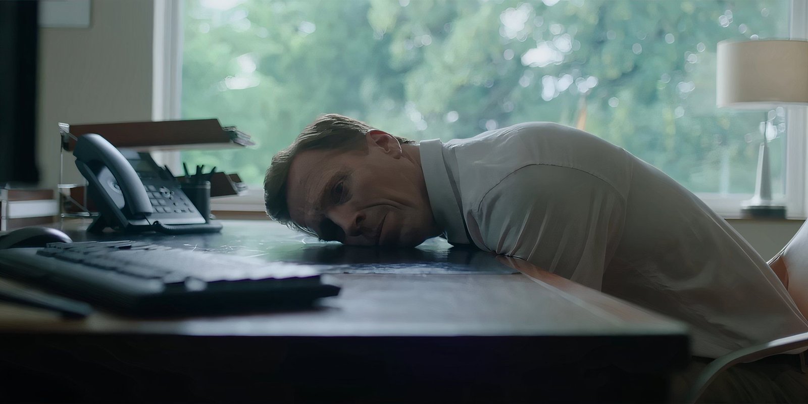Damian Lewis as Peter looking stoic and laying his head on his desk in The Radleys