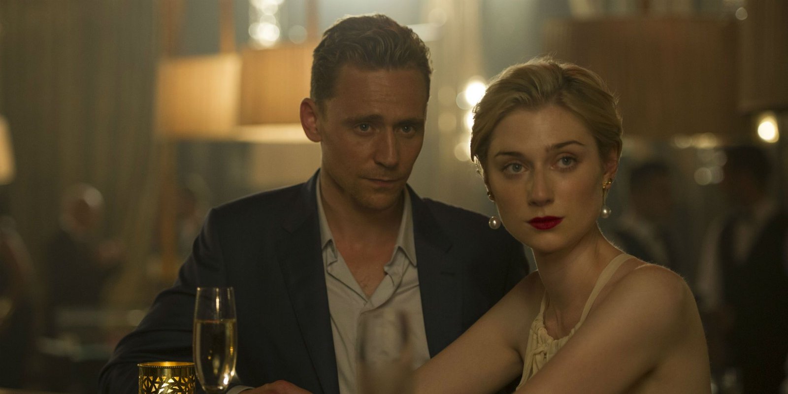 Tom Hiddleston and Elizabeth Debicki look off at someone in a bar in The Night Manager