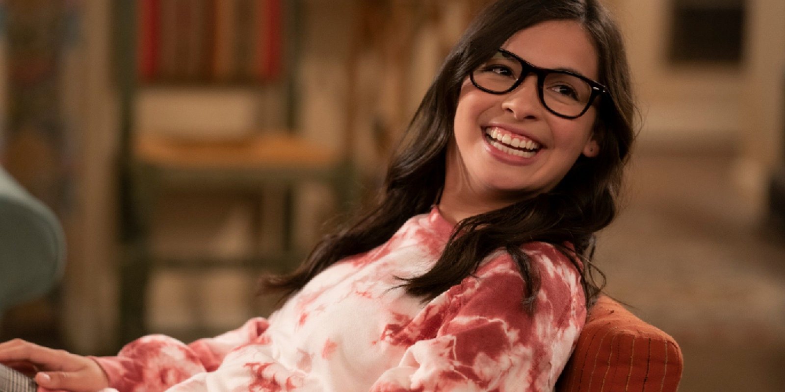 Isabella Gomez as Elena smiling as she leans back in a chair in One Day At A Time