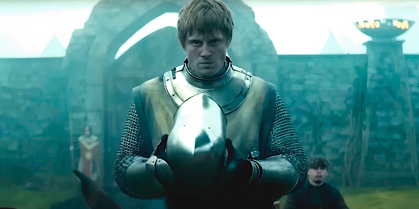 A knight wears a grim countenance as he prepares to put on his helmet in a scene from A Knight of the Seven Kingdoms