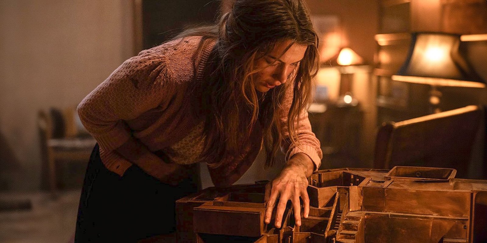 Chloe East as Sister Paxton holding her stomach in pain while looking at a miniature in Heretic