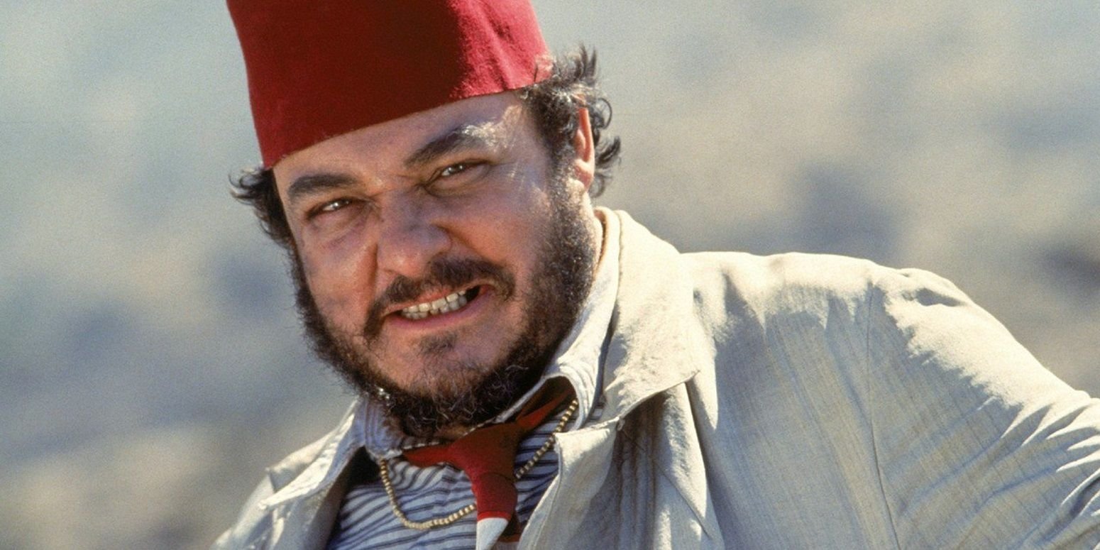 Sallah (John Rhys-Davies) stands smiling in a red fez in Indiana Jones and the Last Crusade.