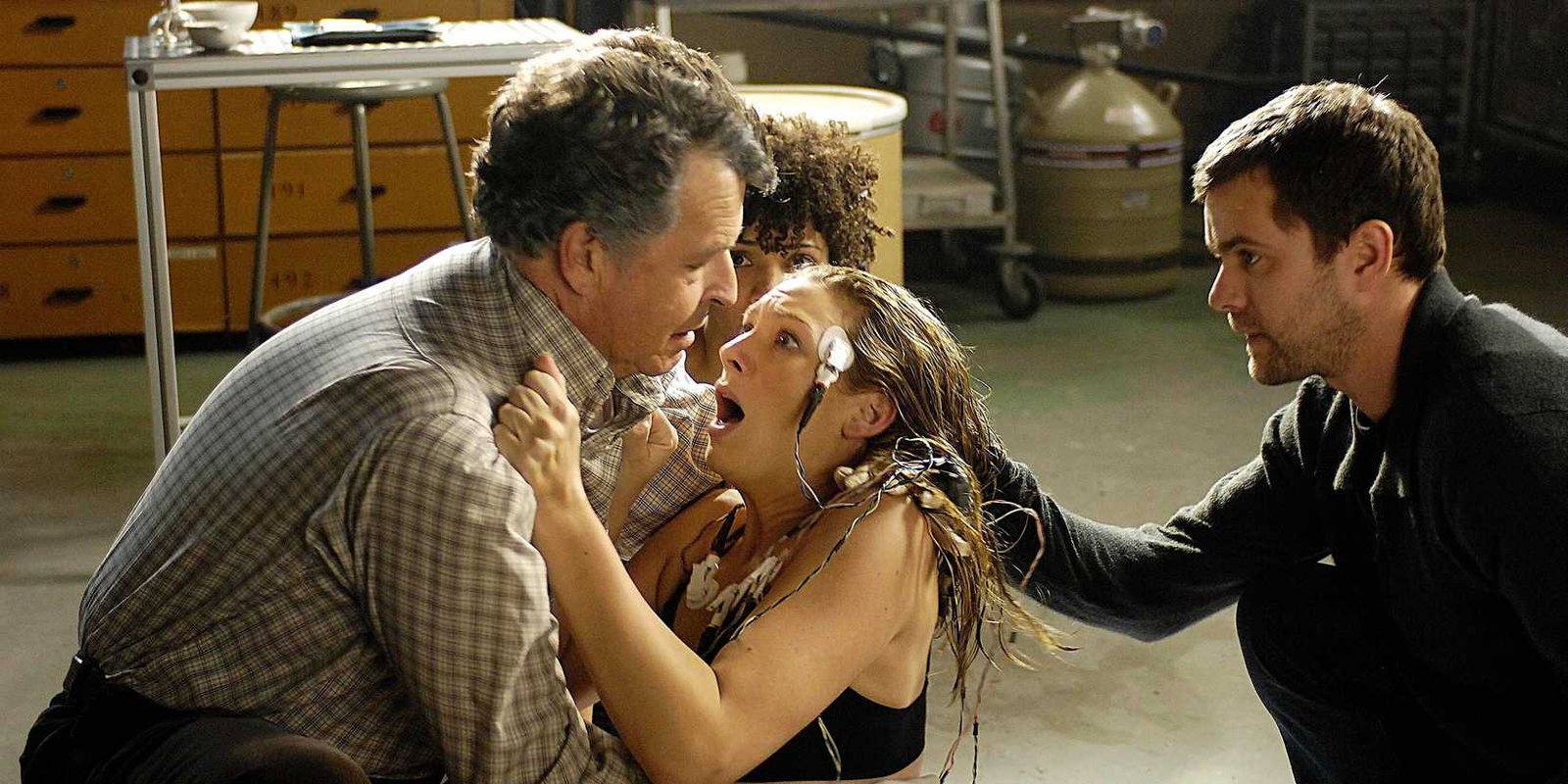 A character gasps for air while wearing wires on her head and clutching another character in Fringe