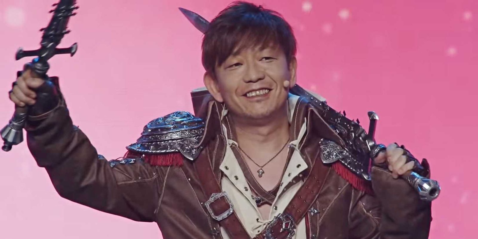 Yoshi-P smiles and waves a sword while wearing a Viper cosplay from Final Fantasy 14.